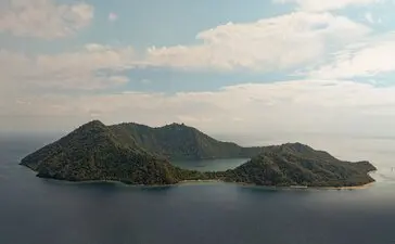 Drone view of Satonda Island's volcanic landscape rising from calm waters at Amanwana, Indonesia.