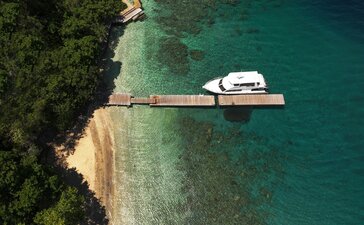 Wooden jetty extending into turquoise waters at Amanwana, Indonesia, with a white boat moored alongside, shot from above.