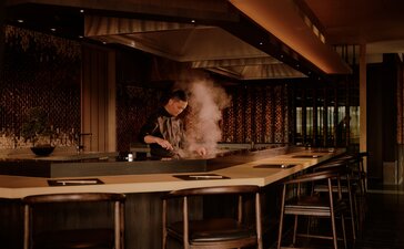 Spa therapist preparing treatments at a wooden table within Aman Bangkok, Thailand.