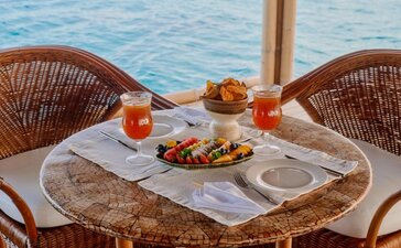Floating bar dining table at Amanpulo with woven chairs, tropical cocktails and fresh fruit overlooking turquoise waters.