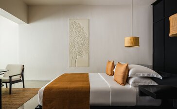 Amansara suite bedroom with wooden bed, neutral tones, and contemporary art.