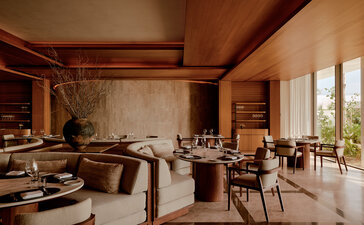 Warm-toned indoor living space at Amanvari with wooden furnishings and natural light from large windows.