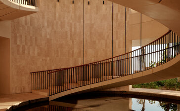 Curved wooden staircase at Amanvari, Mexico, with warm terracotta walls and minimalist design.