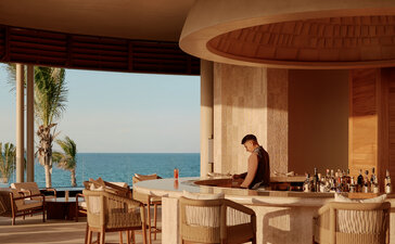 Amanvari's lounge bar with curved wooden architecture, comfortable seating, and expansive views over the Mexican landscape at sunset.