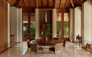 Dining area at Amanyara villa with wooden ceiling, stone flooring, and floor-to-ceiling windows overlooking tropical gardens.