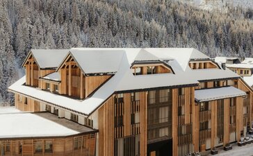 Aman Rosa Alpina resort exterior with wooden architecture set against snow-covered Alpine mountains.