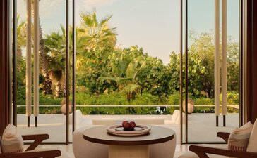 Living area at Amanvari with circular fireplace, mid-century chairs, and views across the estuary to palm trees.