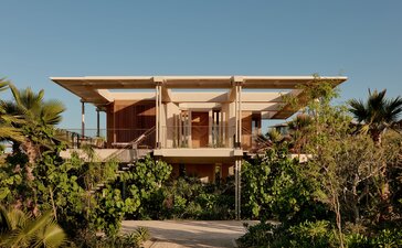Horizon Casita at Amanvari, a modernist pavilion with wooden beams and stone walls, elevated on stilts amongst desert vegetation and palm trees in Mexico.
