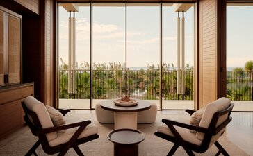 Amanvari Casita living area with floor-to-ceiling windows overlooking Mexican landscape, two modern chairs and round table.