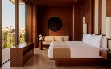 Amanvari principal bedroom with terracotta walls, wooden furnishings, and expansive windows overlooking the Mexican landscape.