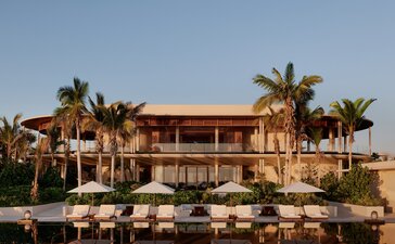 Casa Grande at Amanvari, a sand-coloured residence with palm trees and poolside loungers at sunset, Mexico.