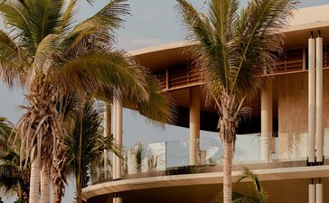Casa Grande at Amanvari, a two-storey wooden residence with palm trees, set against a cloudy sky in Mexico.