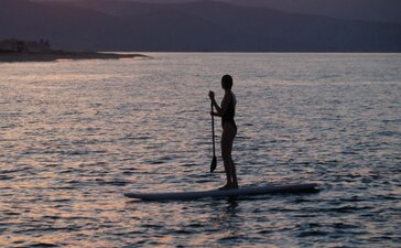 Silhouetted figure paddleboarding on calm waters at sunset, mountains beyond, at Amanvari, Mexico.