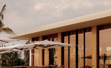 Amanvari villa with wooden facade and terrace overlooking tropical landscape at sunset.