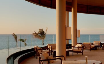 Amanvari's lounge bar at dusk, with curved architecture framing a calm sea view and wooden furnishings.