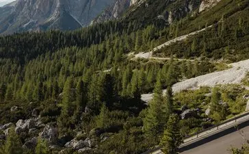 Cyclist on winding mountain road with peaks and forest at Aman Rosa Alpina resort.
