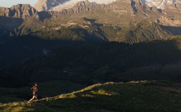 Runner on a mountain trail at Aman Rosa Alpina resort, with Alpine peaks beyond.