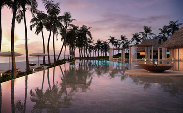 Nura Beach Club at dusk with palm trees reflected in still water, lit buildings beyond.