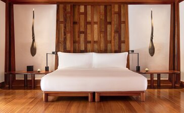 Amanpuri bedroom with wooden headboard feature, pendant lights, and parquet flooring.