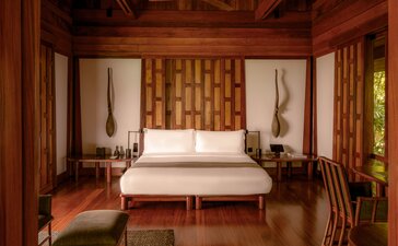 Amanpuri pavilion bedroom with teak wood panelling, central bed, and soft bedside lighting.