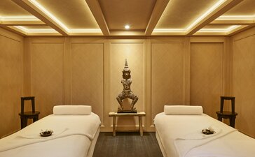 Salle de traitement du spa à Aman Le Mélézin, deux lits de massage blanc crème face à face dans un espace aux tons dorés apaisants.