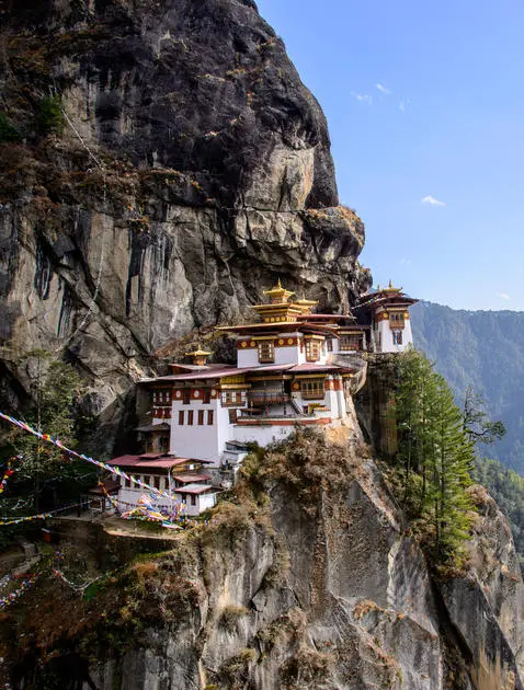 Tiger's Nest monastery clinging to a cliff edge at Amankora, Bhutan, with golden roofs and red-painted walls against mountain backdrop.