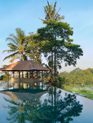 Amandari's main pool pavilion surrounded by tropical palms and lush greenery, with calm water reflecting the structure and landscape.