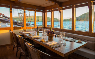 Dining area at Amandira with wooden furnishings, large windows overlooking water and mountains.