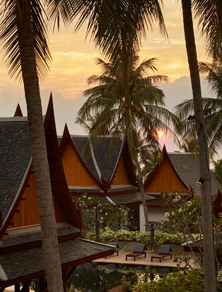 Golden sunset over Amanpuri villa with traditional Thai architecture and palm trees.
