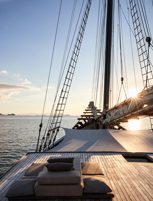 Sailing vessel deck with view along mast towards distant island at Amandira, golden hour light.
