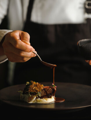 Hand drizzling sauce over a plated dish at Aman Kyoto's Christmas dinner service.
