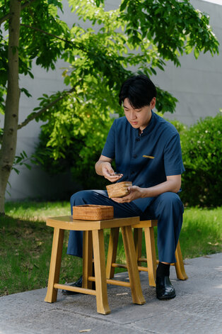 Young man sitting on wooden stool at Amanyangyun, tending to an emperor tree seedling.