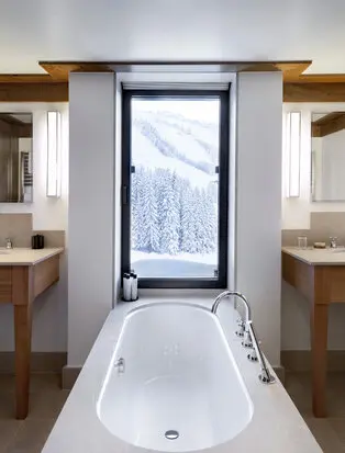 Principal bedroom bathroom at Aman Le Mélézin with freestanding bath and mountain views through window.