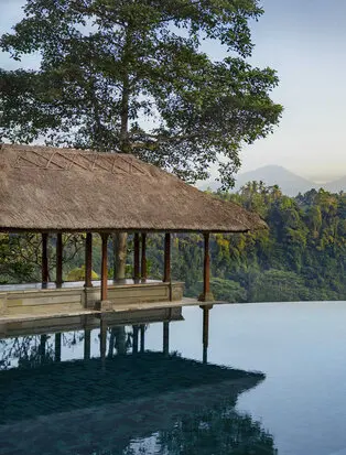 Amandari's infinity pool pavilion reflects in still water, surrounded by Balinese forest at dawn.