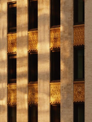 Fachada do Aman New York com janelas iluminadas ao entardecer, padrão geométrico de luz e sombra.