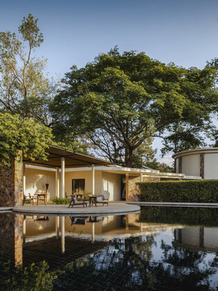 Amansara pavilion reflected in still water at dusk, surrounded by tropical gardens.