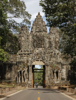 Stone gateway with intricate carved details framed by trees at Amansara, Cambodia.