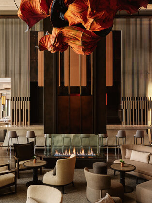 Lounge do Aman New York com luminária esculpida em tons de laranja suspenso acima de assentos em pele neutra.