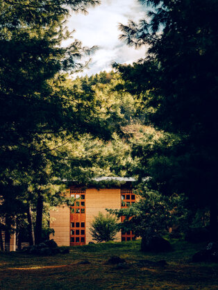 Amankora's Paro Lodge exterior at dusk, with warm-lit wooden structure nestled amongst dense green trees.