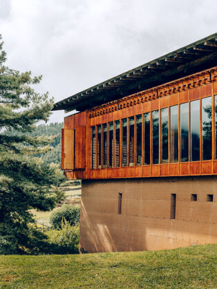 Gangtey Lodge exterior with traditional orange wooden architecture and stone base, surrounded by green landscape in Bhutan.