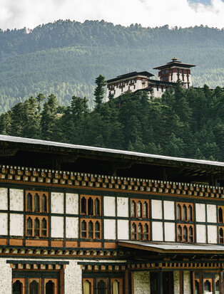 Traditional Bhutanese architecture with mountain monastery visible beyond forested peaks at Amankora, Bumthang.
