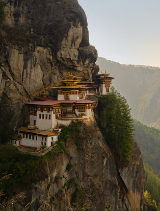 Tiger's Nest monastery perched on a cliff edge in Bhutan's Paro Valley, with golden roofs and traditional architecture set against forested mountains.