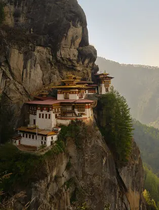 Tiger's Nest monastery perched on a cliff edge in Bhutan's Paro Valley, with golden roofs and traditional architecture set against forested mountains.