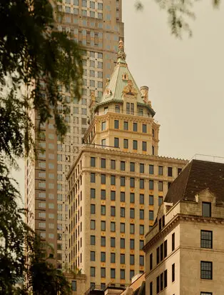 Fachada exterior del Aman New York, edificio histórico con torre dorada rodeado de rascacielos.