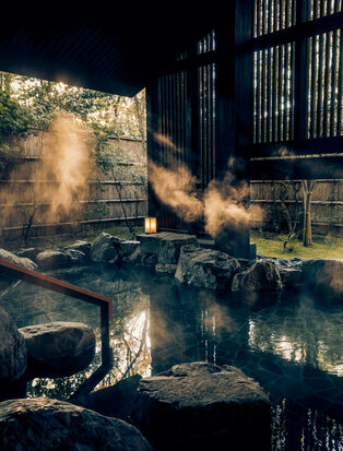 Steaming onsen pool at Aman Kyoto with warm water and traditional wooden architecture in soft golden light.