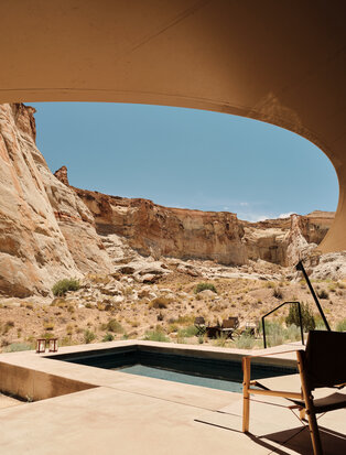 Wooden bench facing plunge pool at Amangiri pavilion, framed by canyon rock formations under clear sky.