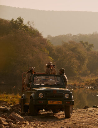 Safari vehicle on a dusty track at Aman-i-Khas, with forested hills in the hazy distance.