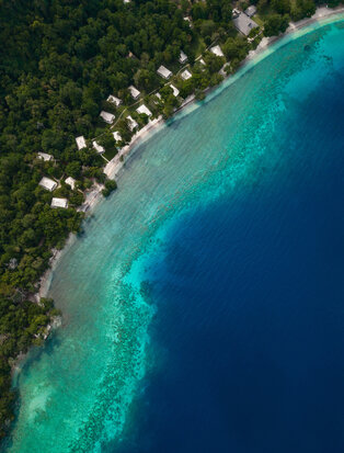 Aerial view of Amanwana's shoreline with white villas nestled along turquoise waters and dense forest.