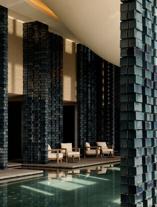 Spa pool at Aman Tokyo with black tiled columns, soft lighting, and serene water feature.