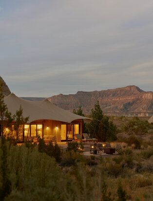 Amangiri resort's illuminated pavilion at dusk with desert mountains beyond.